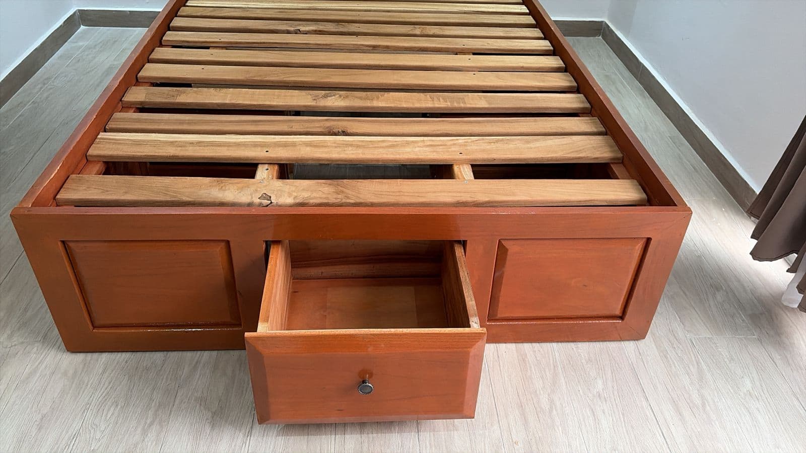 Foot of the custom wood bed with its built-in storage drawer open